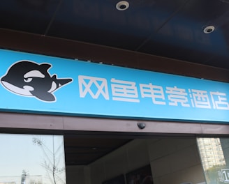A building entrance features a vibrant blue sign with white Chinese characters and a stylized orca logo in black and white. The overall appearance suggests an establishment focused on eSports or digital activities.